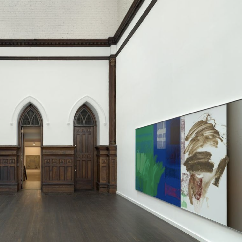 An image of a gallery room. There is two church doors int he back, and a blue and green art work in the foreground.
